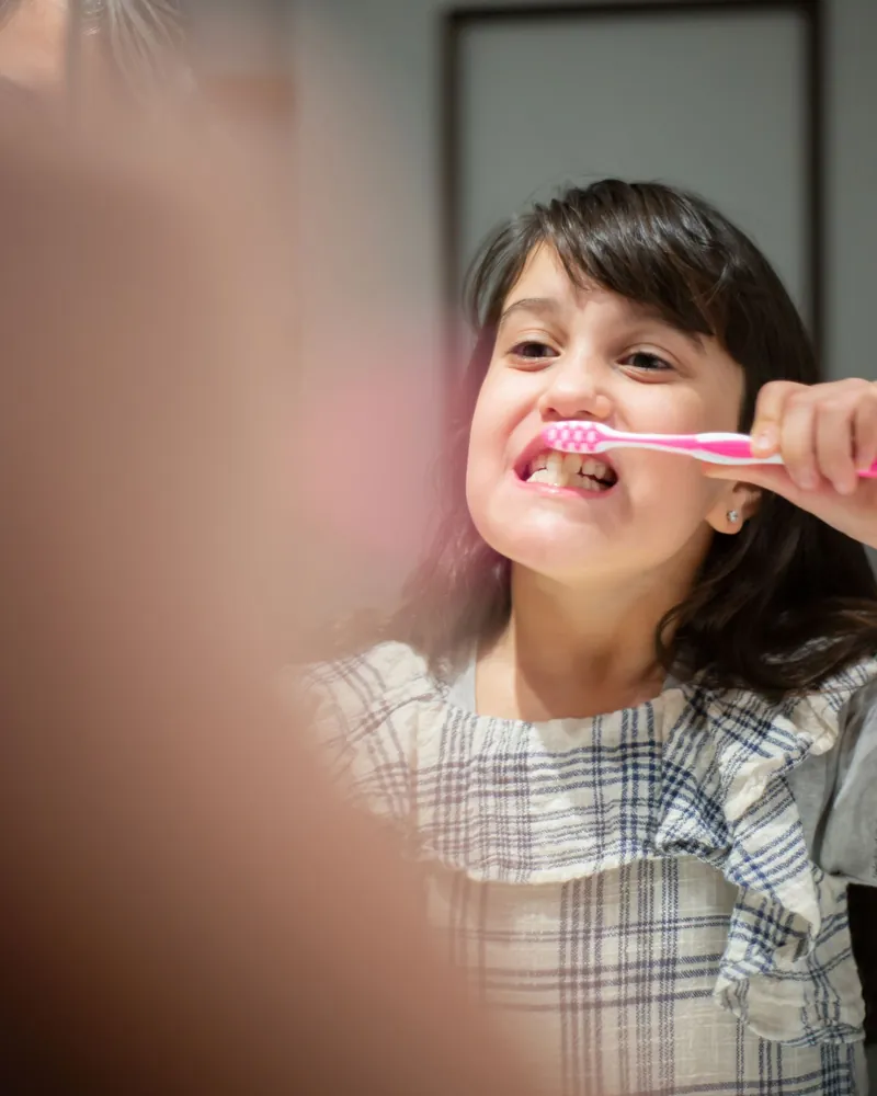 Uma menina escovando os dentes diante do espelho