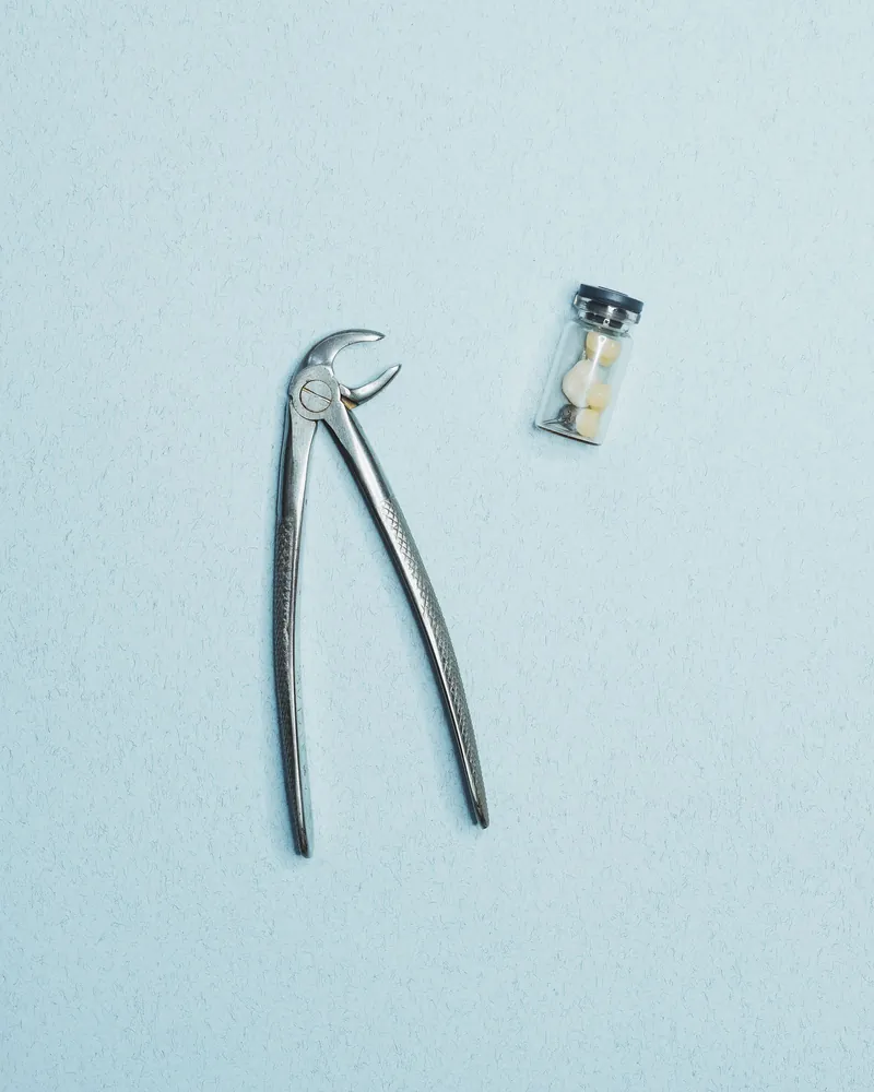 Um fórceps odontológico ao lado de um dente, sobre fundo claro