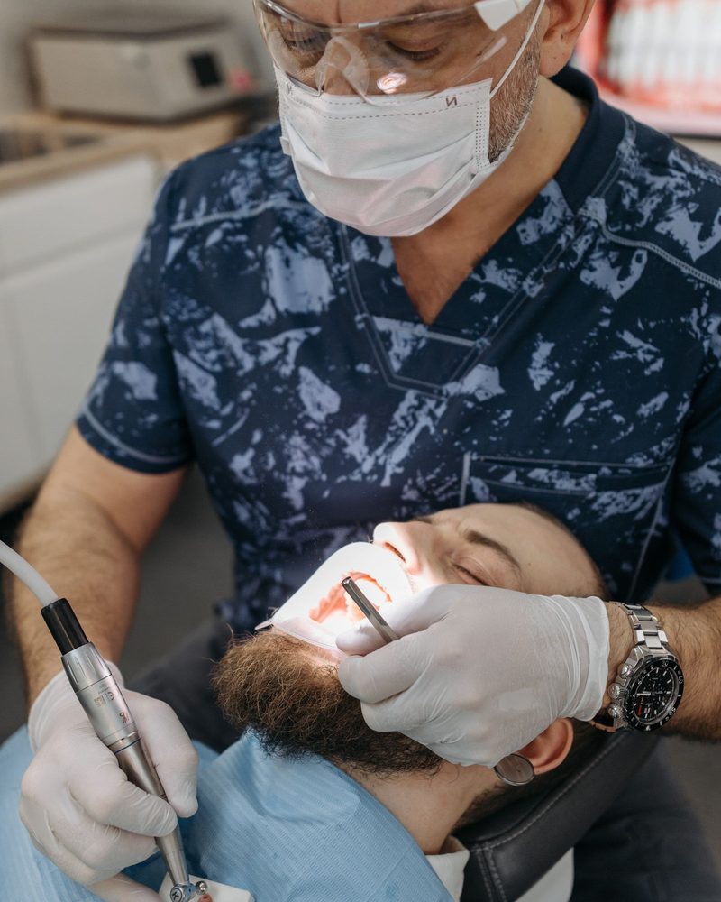 Imagem ilustrativa: dentista de máscara, óculos e luvas atendendo um paciente na cadeira