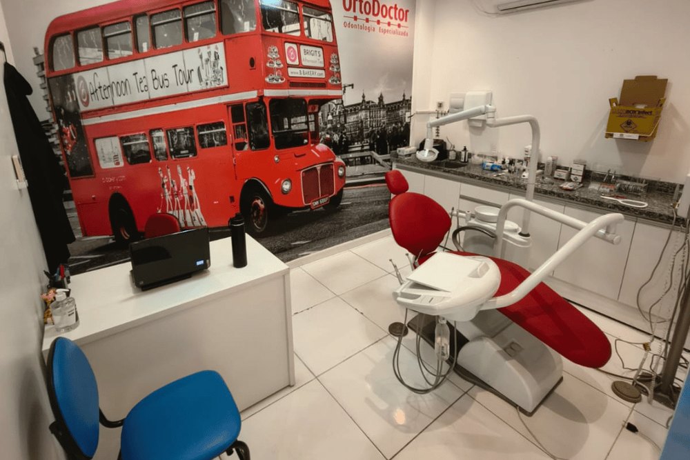 Um consultório, com a cadeira vermelha e o painel do ônibus de Londres — OrtoDoctor São José, dentista no São José Operário, Manaus