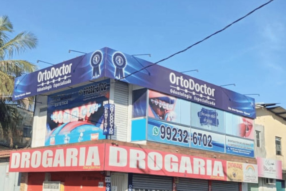 A fachada: a esquina, com o letreiro azul no 1º andar, em cima da drogaria — OrtoDoctor São José, dentista no São José Operário, Manaus